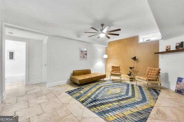 living area featuring ceiling fan, wood walls, and baseboards