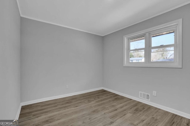 empty room featuring crown molding, wood finished floors, visible vents, and baseboards