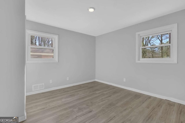 unfurnished room featuring baseboards, visible vents, and wood finished floors