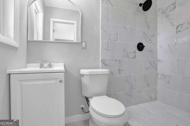 bathroom with toilet, tiled shower, vanity, and baseboards