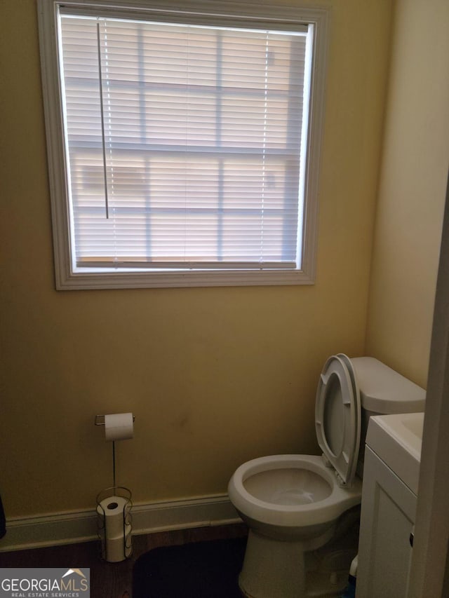 half bath featuring vanity, toilet, and baseboards