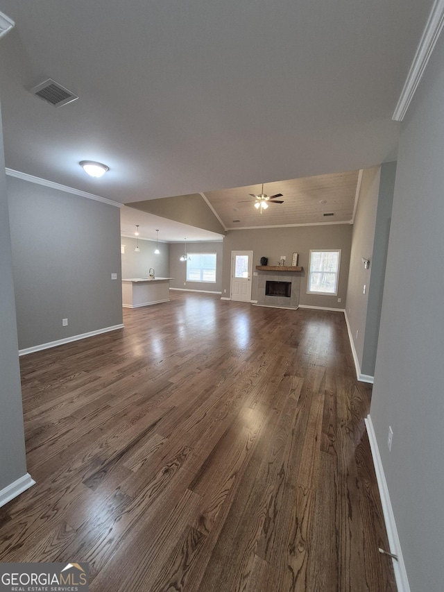 unfurnished living room featuring ceiling fan, a fireplace, dark wood finished floors, and crown molding