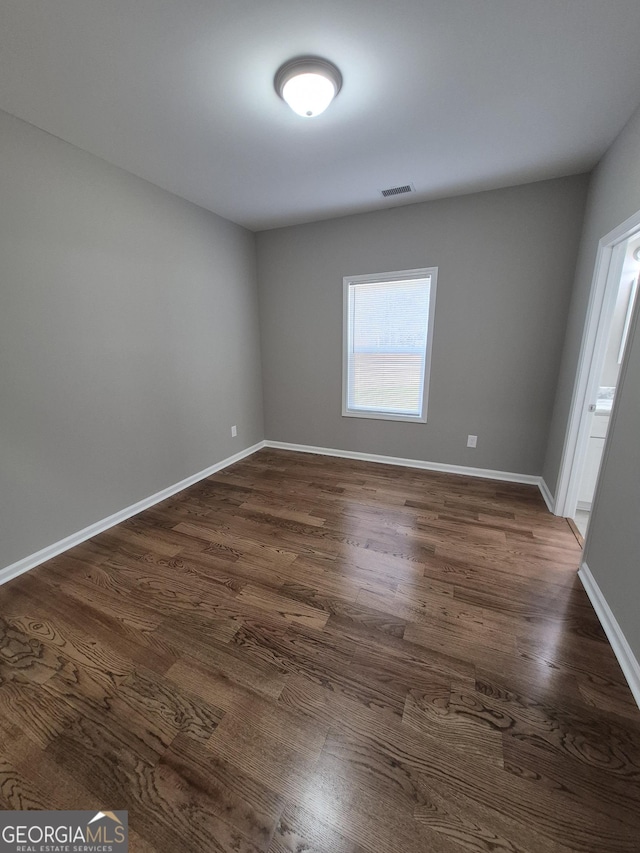 spare room featuring visible vents, dark wood finished floors, and baseboards