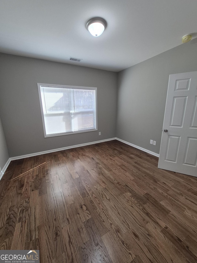 unfurnished room featuring dark wood-type flooring, visible vents, and baseboards