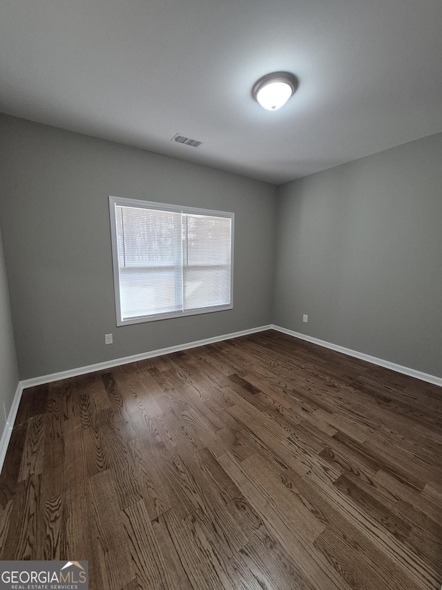 empty room with visible vents, dark wood finished floors, and baseboards