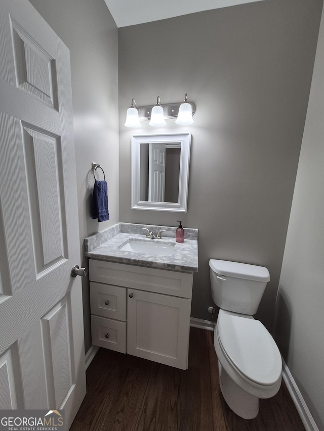 half bathroom featuring toilet, wood finished floors, vanity, and baseboards