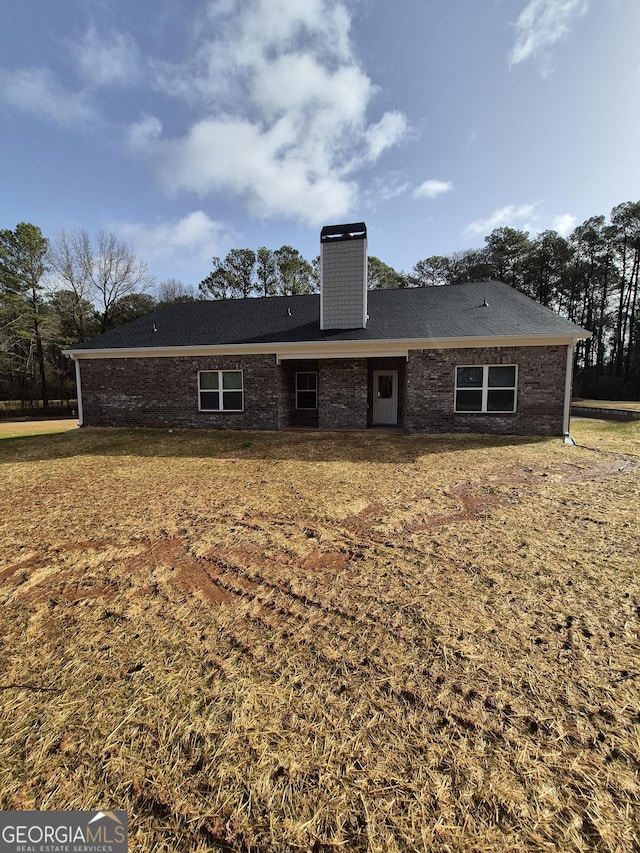 back of property featuring brick siding, a yard, and a chimney