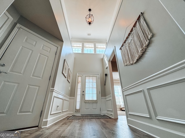 entrance foyer featuring a decorative wall, wood finished floors, visible vents, ornamental molding, and wainscoting