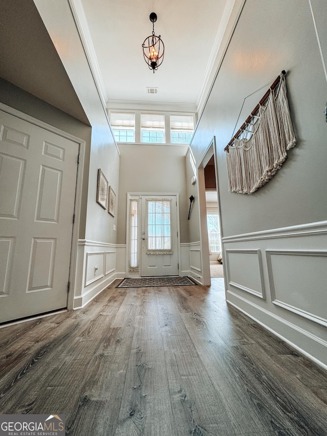 entryway featuring visible vents, a wainscoted wall, ornamental molding, wood finished floors, and a notable chandelier