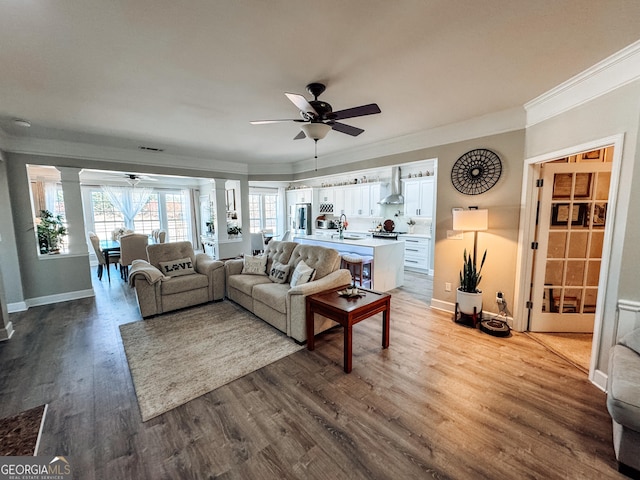living area featuring decorative columns, a ceiling fan, ornamental molding, wood finished floors, and plenty of natural light