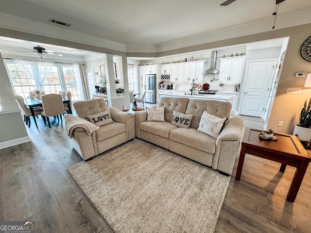 living room with visible vents, dark wood finished floors, a ceiling fan, and ornamental molding