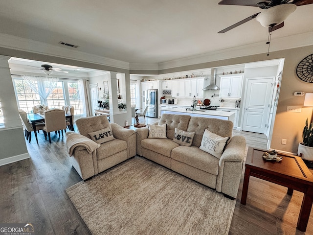 living room featuring wood finished floors, visible vents, crown molding, and decorative columns