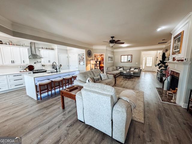 living room with ornamental molding, a fireplace, ceiling fan, and wood finished floors
