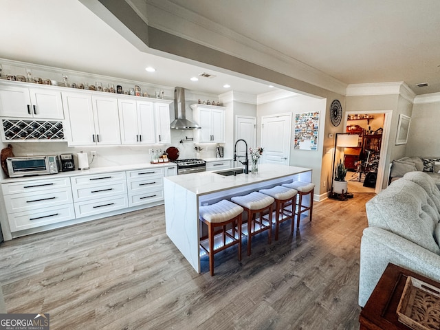 kitchen with a breakfast bar area, a sink, open floor plan, light wood-type flooring, and wall chimney exhaust hood
