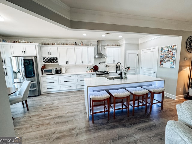kitchen with wood finished floors, a sink, white cabinetry, appliances with stainless steel finishes, and wall chimney exhaust hood