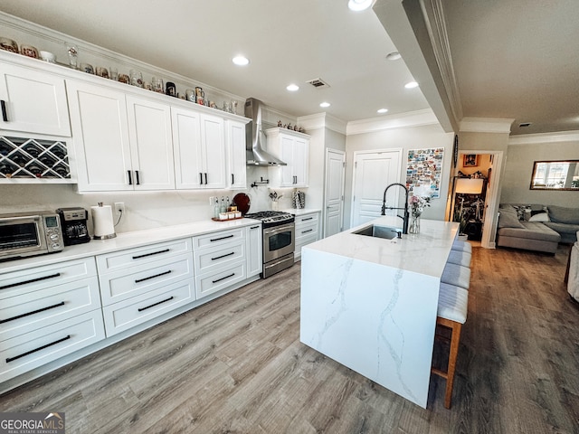 kitchen featuring a sink, wall chimney range hood, light wood-type flooring, and stainless steel range with gas stovetop