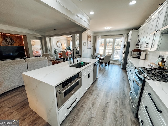 kitchen with ornate columns, stainless steel appliances, a sink, and wood finished floors