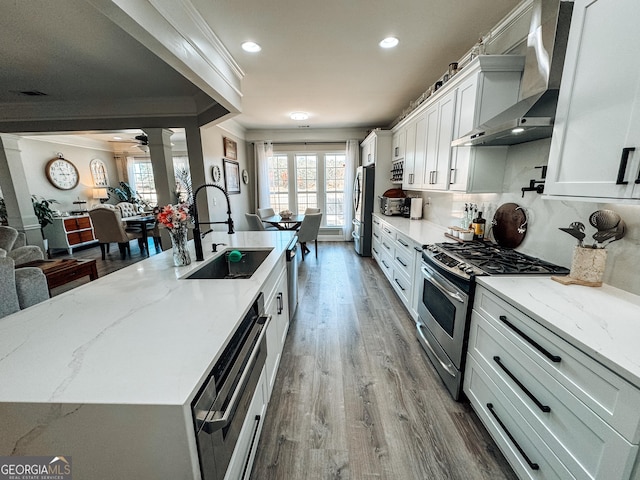 kitchen featuring appliances with stainless steel finishes, a sink, wood finished floors, a large island with sink, and wall chimney exhaust hood