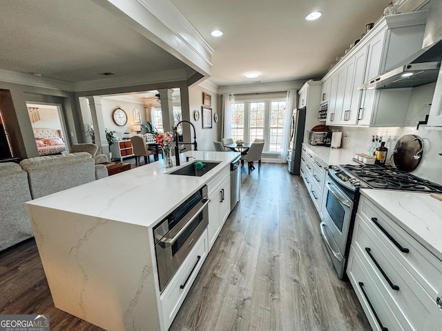 kitchen featuring stainless steel appliances, a sink, ornamental molding, wall chimney range hood, and ornate columns