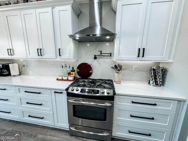 kitchen featuring stainless steel range with gas cooktop, dark wood finished floors, decorative backsplash, white cabinetry, and wall chimney range hood