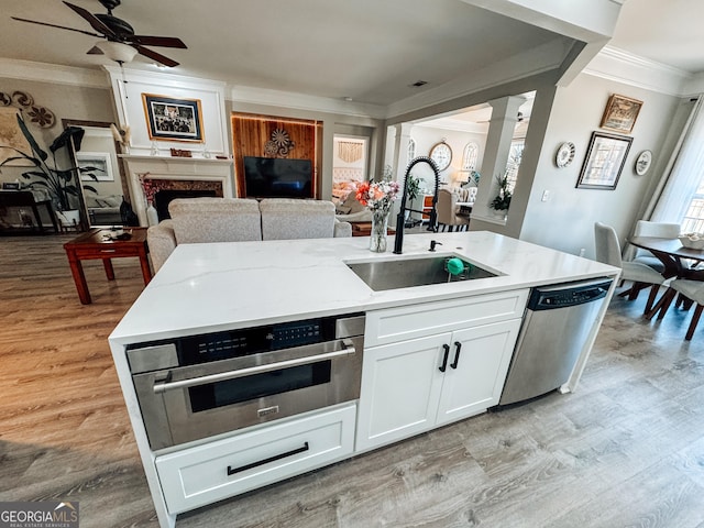 kitchen featuring decorative columns, dishwasher, ornamental molding, open floor plan, and a sink