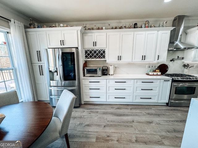 kitchen featuring wall chimney range hood, white cabinetry, stainless steel appliances, and light wood-style floors