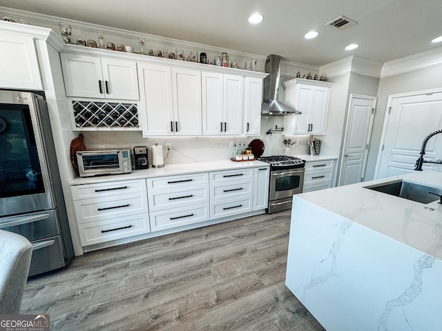 kitchen with a toaster, visible vents, stainless steel appliances, wall chimney range hood, and a sink