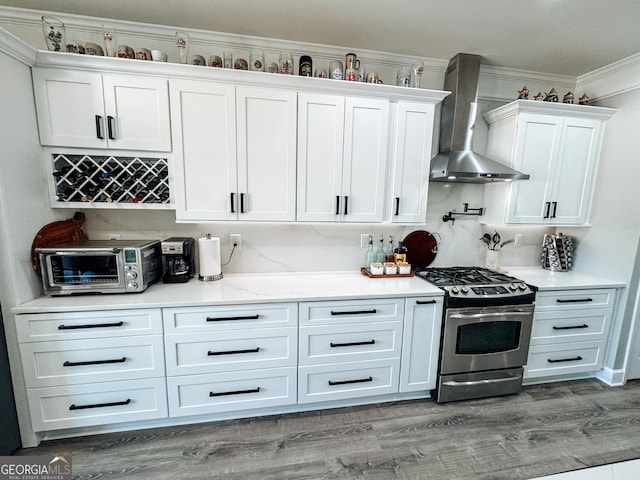 kitchen featuring stainless steel gas range, white cabinetry, light wood-style flooring, and wall chimney range hood