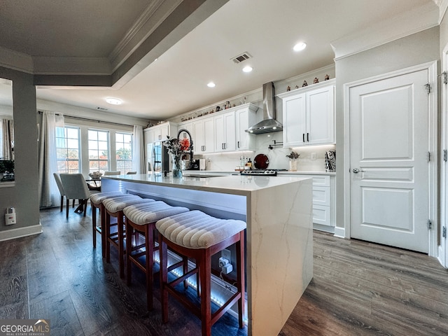 kitchen featuring visible vents, ornamental molding, dark wood-style flooring, a center island, and wall chimney range hood