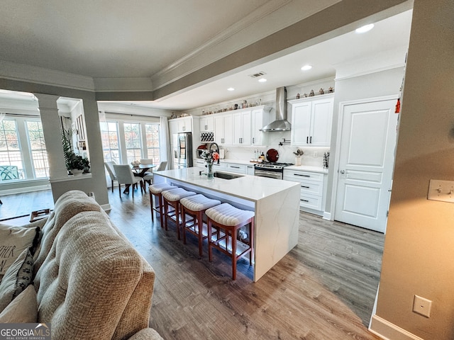 kitchen featuring wall chimney exhaust hood, appliances with stainless steel finishes, ornamental molding, a kitchen breakfast bar, and a sink