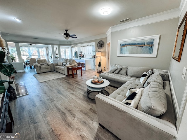 living area featuring baseboards, visible vents, a ceiling fan, ornamental molding, and light wood-type flooring