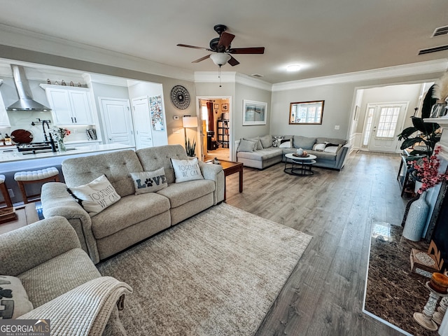 living area featuring light wood finished floors, a ceiling fan, and crown molding