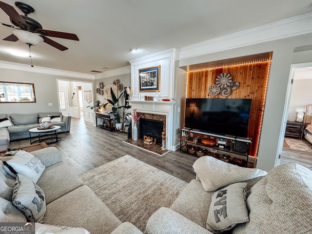 living room with ornamental molding, ceiling fan, a premium fireplace, and wood finished floors