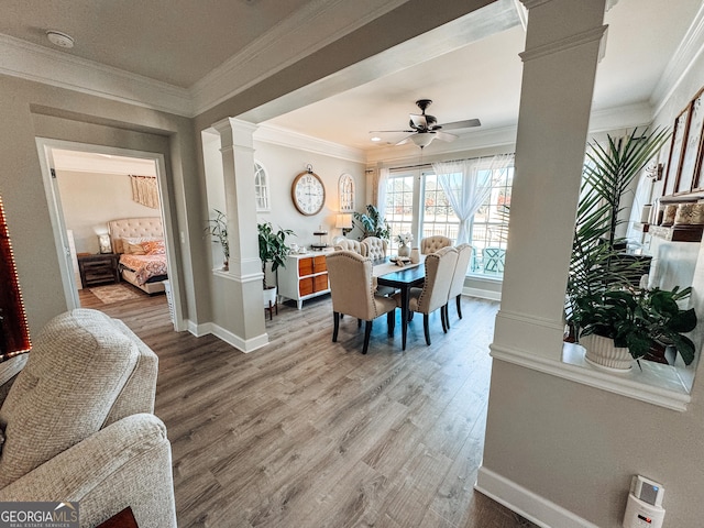 dining room featuring ceiling fan, wood finished floors, baseboards, decorative columns, and crown molding
