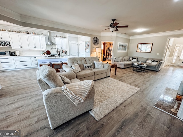 living area featuring wood finished floors, a ceiling fan, and crown molding