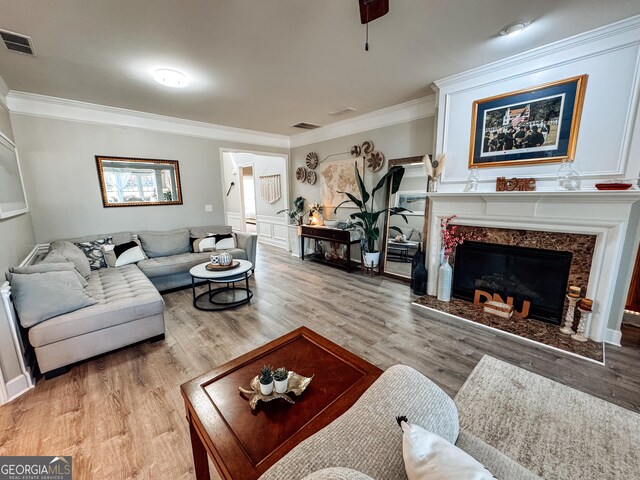 living area featuring light wood finished floors, a fireplace, visible vents, and ornamental molding