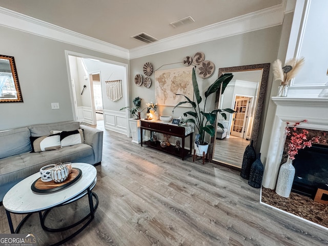 living area featuring wainscoting, visible vents, crown molding, and wood finished floors