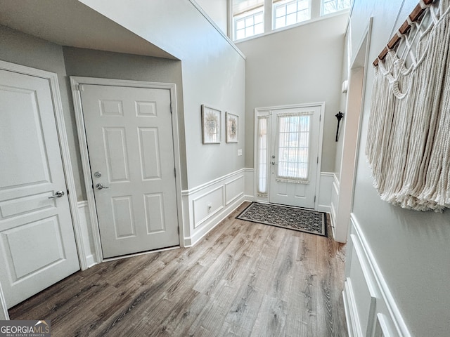 foyer entrance featuring a wainscoted wall, a decorative wall, a high ceiling, and wood finished floors