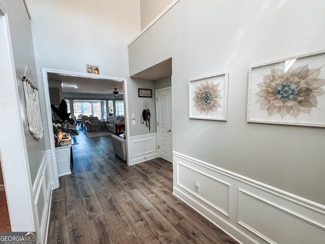 hall featuring dark wood-style floors, a wainscoted wall, and a decorative wall