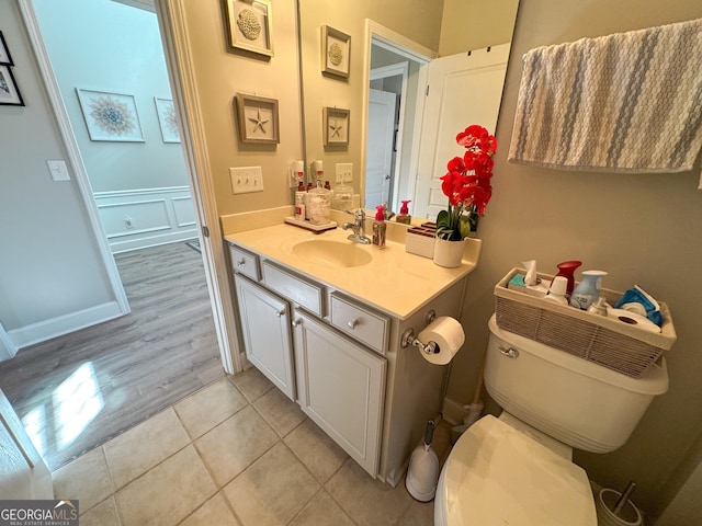 bathroom featuring a wainscoted wall, a decorative wall, toilet, vanity, and tile patterned flooring