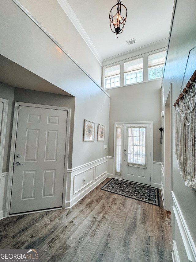entryway with visible vents, ornamental molding, wood finished floors, and wainscoting