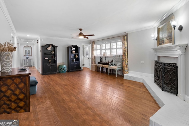 living area with a fireplace with raised hearth, ornamental molding, hardwood / wood-style flooring, and a ceiling fan