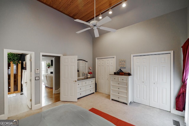 bedroom with high vaulted ceiling, light carpet, visible vents, multiple closets, and track lighting