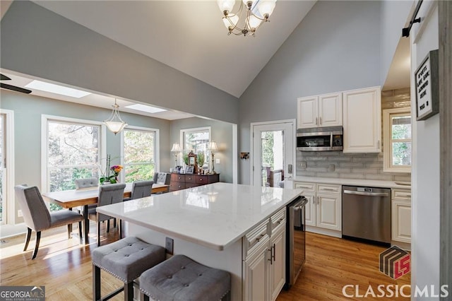 kitchen featuring wine cooler, a center island, hanging light fixtures, stainless steel appliances, and light wood-type flooring