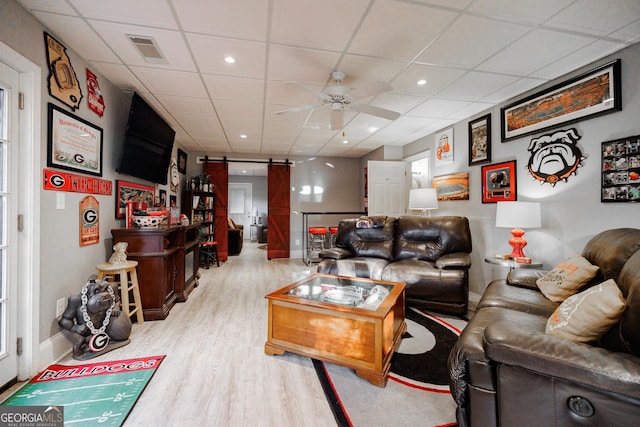 living area featuring a barn door, visible vents, a ceiling fan, wood finished floors, and a paneled ceiling