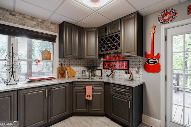 bar featuring indoor wet bar, decorative backsplash, light wood-style floors, a sink, and baseboards