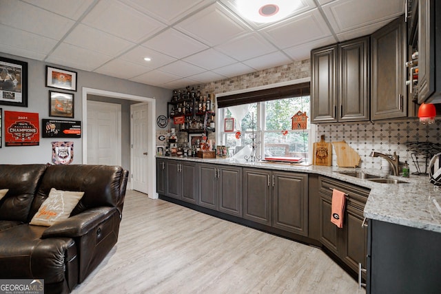 kitchen with light stone counters, a sink, light wood-style floors, open floor plan, and tasteful backsplash