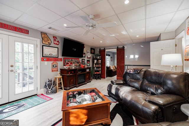 living room with a paneled ceiling, a barn door, visible vents, and wood finished floors