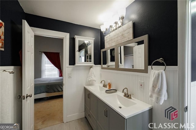 bathroom with a wainscoted wall, double vanity, a sink, and ensuite bathroom