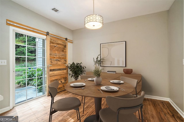 dining room featuring a barn door, wood finished floors, visible vents, and baseboards